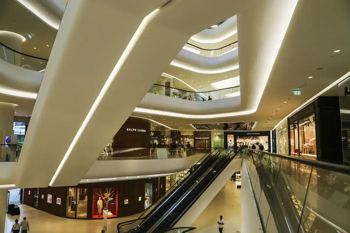 Wide shot of an empty indoor mall corridor with generic storefronts and signage placeholders, dimmed lights and a lone shopping trolley near an entrance