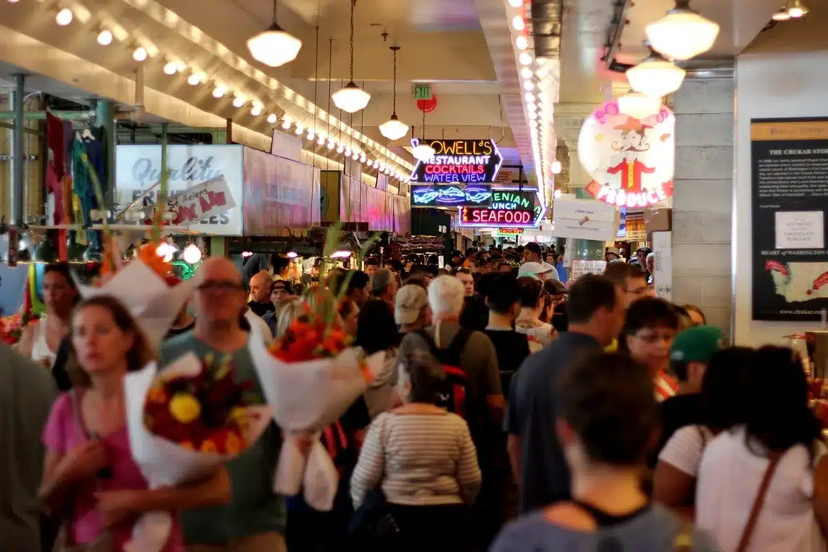 Anonymous shoppers in a blurred crowd passing unbranded store facades under mall lights, motion suggesting activity and anticipation