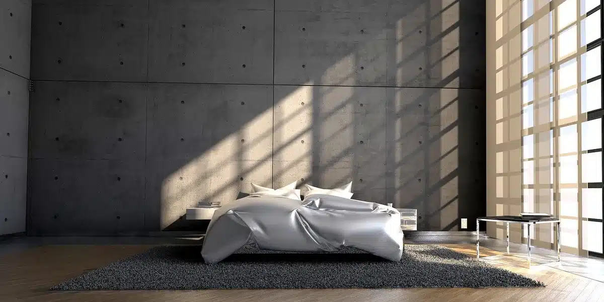 A neutral bedroom scene with a made bed, a generic pet bed at the foot and an open laundry basket of linens nearby