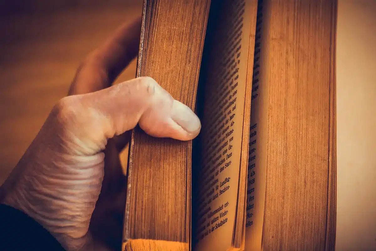 A person’s hands turning a paperback page on a crowded commuter seat, backpack at their feet and blurred station in background