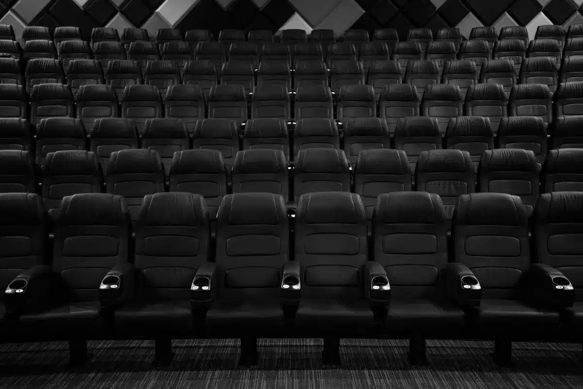 Wide, empty cinema auditorium with a single spotlight on a distant seat, aisle lights glowing