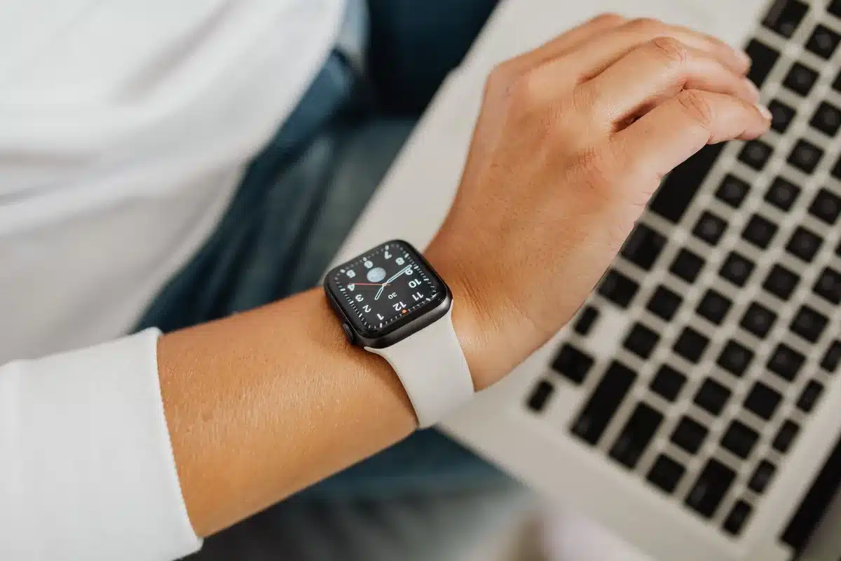 An anonymous wrist wearing a slim, generic smartwatch with a leather-style strap near a cup of coffee on a wooden table, hands blurred and unrecognizable