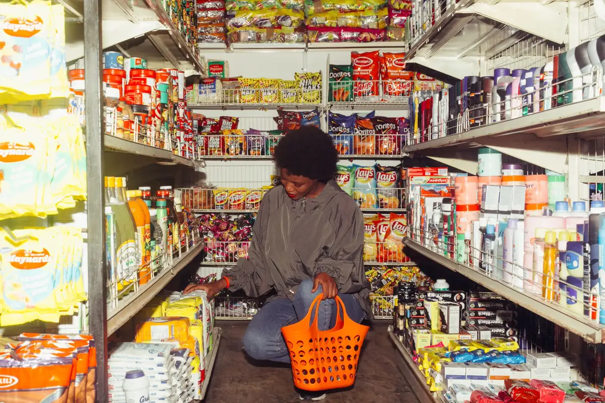 Anonymous shopper pushing an empty wheeled basket past unbranded produce shelves, soft store lighting, no visible faces; focus on basket and stacked fruits