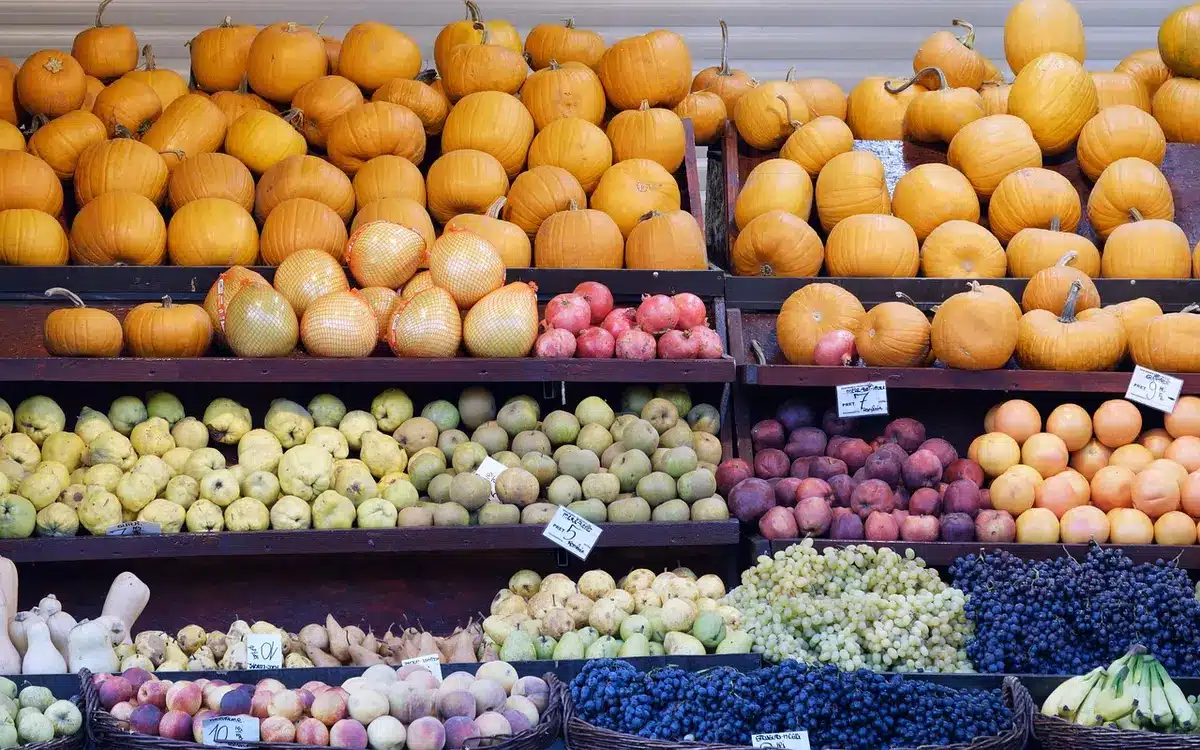 Empty supermarket produce aisle with stacked wooden crates of unbranded fruits and clear generic price tags, fluorescent-lit ceiling and a shopping cart in the aisle