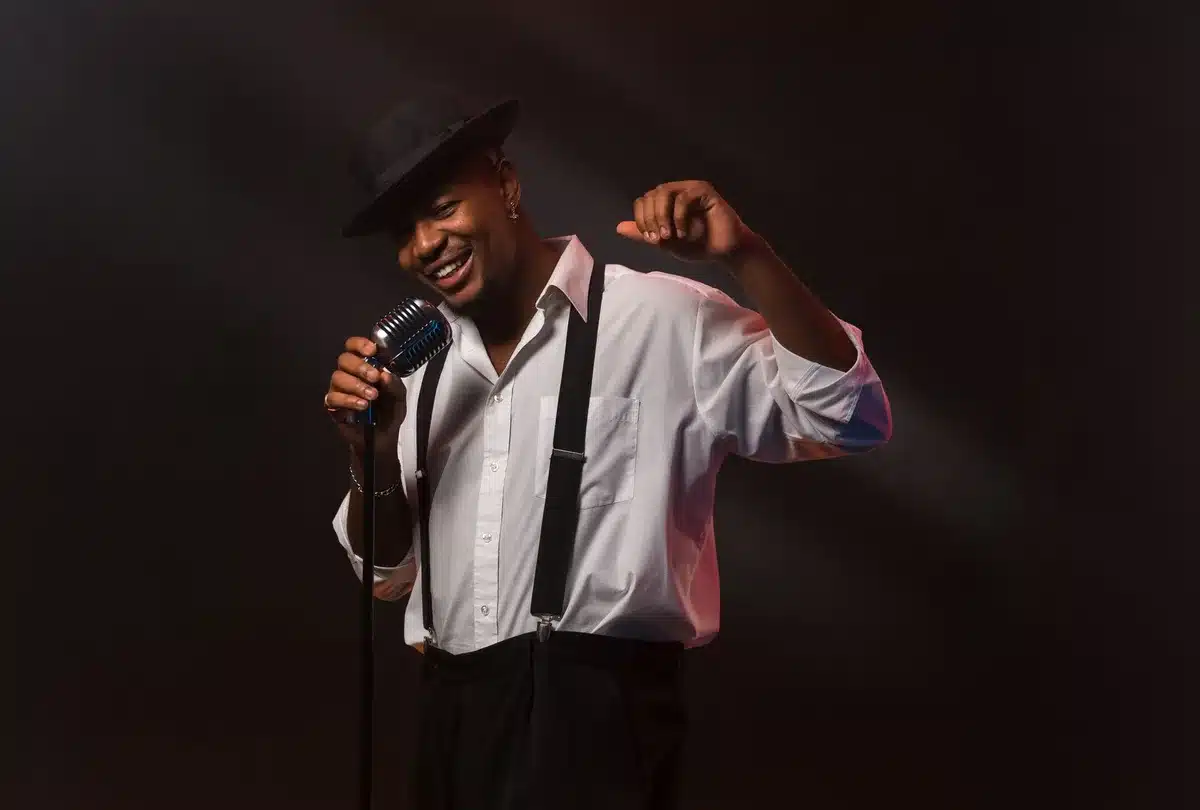 Empty stage with a single vintage microphone under a spotlight, dust motes visible, coiled cable trailing off to the side — symbolic music/voice scene