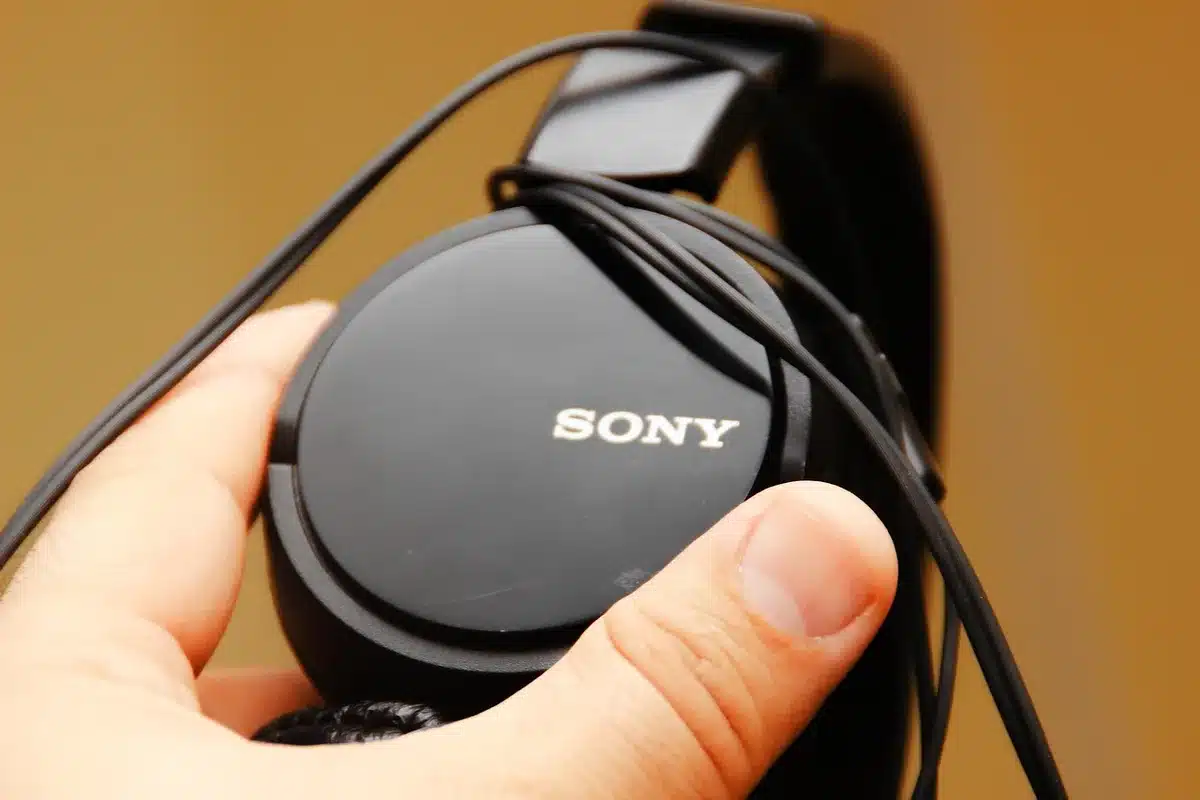 An anonymous person listening with headphones while looking at a tablet, dimly lit interior, focused on audio playback controls